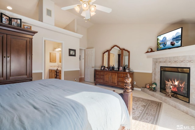 carpeted bedroom with ceiling fan, a fireplace, connected bathroom, and vaulted ceiling