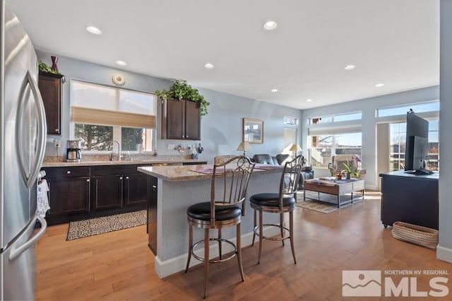 kitchen featuring stainless steel fridge, light stone counters, light hardwood / wood-style flooring, a center island, and a breakfast bar area