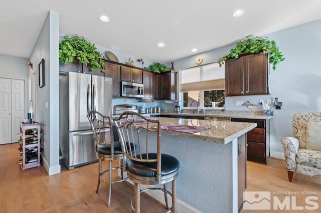 kitchen with dark brown cabinetry, a center island, light hardwood / wood-style flooring, and appliances with stainless steel finishes