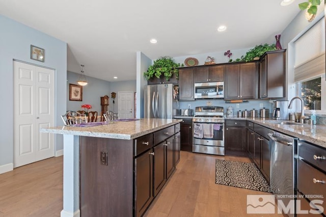 kitchen featuring appliances with stainless steel finishes, dark brown cabinetry, sink, light hardwood / wood-style flooring, and a center island