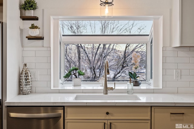 kitchen with light stone countertops, dishwasher, sink, cream cabinets, and decorative backsplash