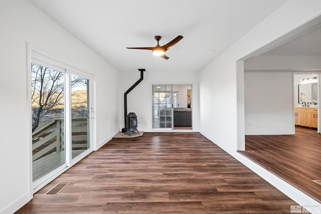 unfurnished living room with a wood stove, ceiling fan, and dark wood-type flooring