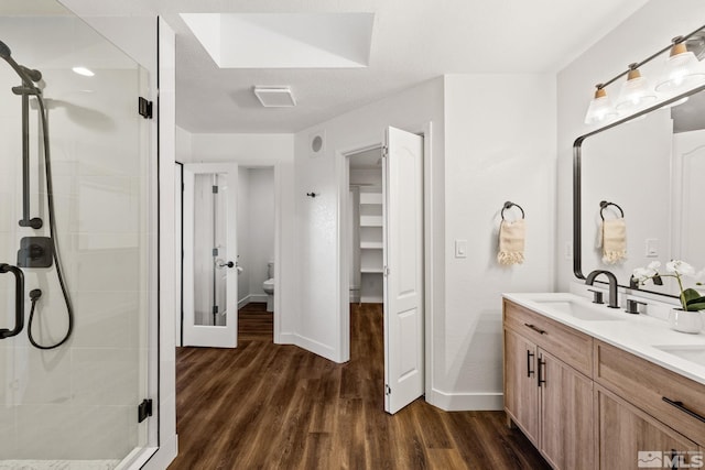 bathroom featuring a skylight, walk in shower, wood-type flooring, toilet, and vanity