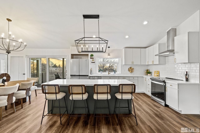 kitchen featuring wall chimney range hood, white cabinetry, white fridge, a kitchen island, and range with electric stovetop