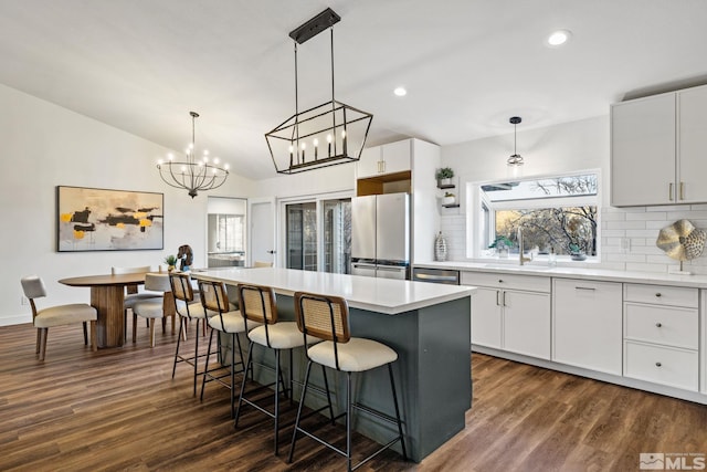 kitchen with white cabinets, appliances with stainless steel finishes, tasteful backsplash, decorative light fixtures, and a kitchen island