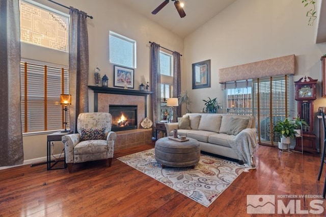 living room with a fireplace, high vaulted ceiling, ceiling fan, and dark wood-type flooring