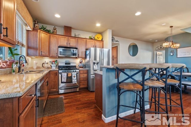 kitchen with a kitchen breakfast bar, stainless steel appliances, sink, dark hardwood / wood-style floors, and hanging light fixtures