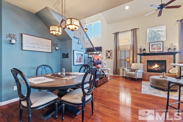 dining area with a tile fireplace, ceiling fan with notable chandelier, and hardwood / wood-style flooring