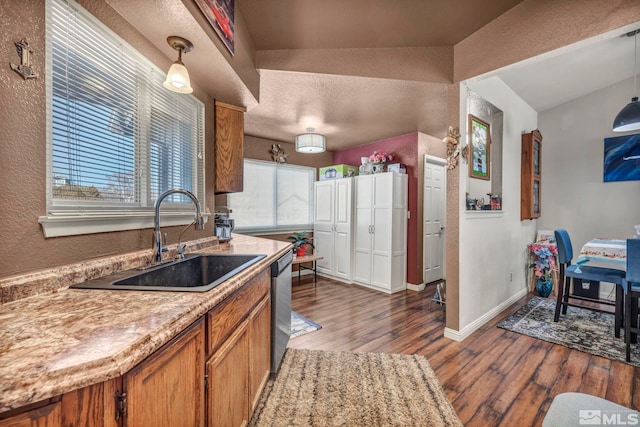 kitchen with dishwasher, lofted ceiling, sink, hanging light fixtures, and hardwood / wood-style flooring