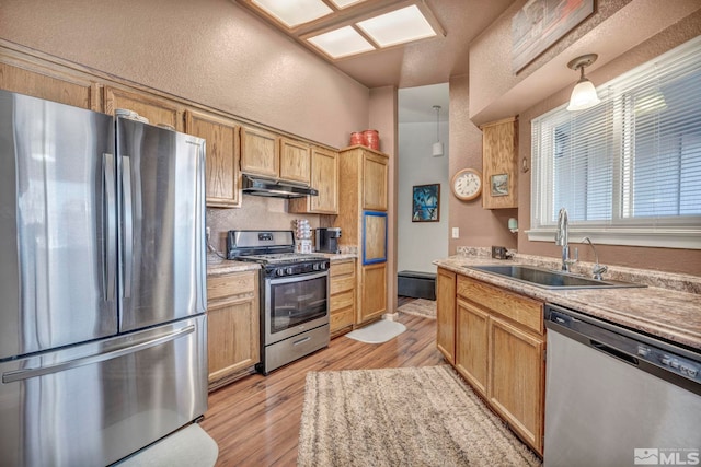 kitchen with sink, hanging light fixtures, light brown cabinetry, appliances with stainless steel finishes, and light hardwood / wood-style floors