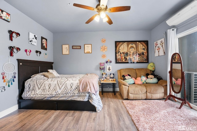 bedroom with hardwood / wood-style flooring, a wall unit AC, and ceiling fan