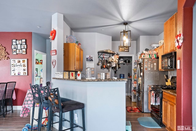 kitchen with kitchen peninsula, dark hardwood / wood-style flooring, a breakfast bar, black appliances, and pendant lighting