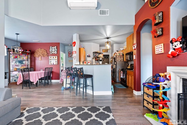 kitchen with a kitchen bar, kitchen peninsula, a wall unit AC, black appliances, and hardwood / wood-style floors