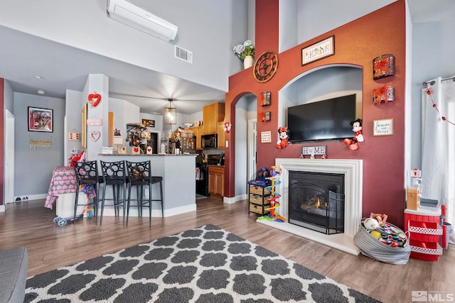 living room featuring wood-type flooring, a towering ceiling, and a wall unit AC