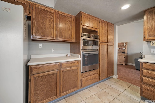 kitchen with light tile patterned floors, stainless steel double oven, and white refrigerator