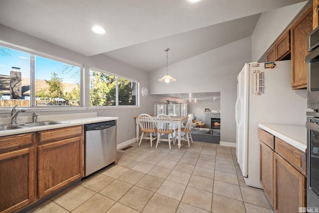 kitchen with sink, hanging light fixtures, vaulted ceiling, stainless steel dishwasher, and a fireplace