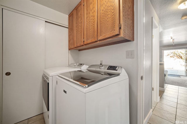 laundry area with washer and dryer, light tile patterned floors, cabinets, and a textured ceiling