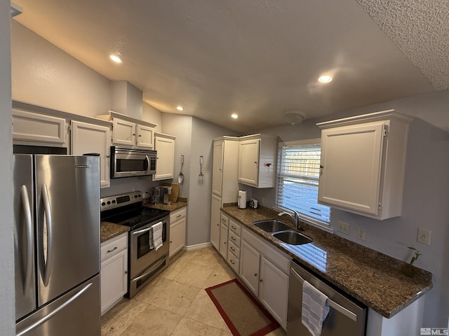 kitchen with dark stone counters, white cabinets, sink, light tile patterned floors, and stainless steel appliances