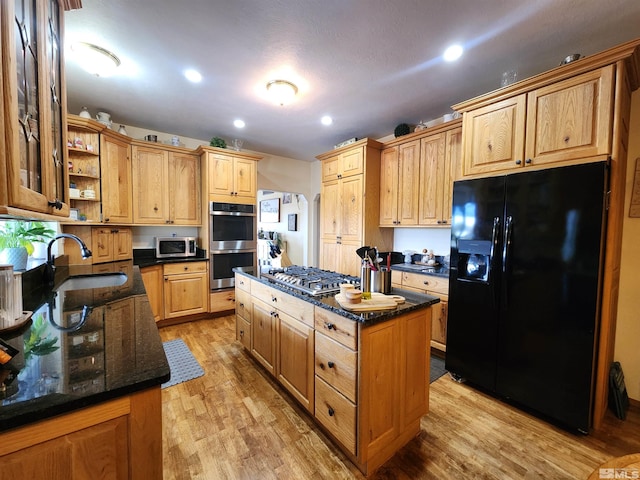 kitchen featuring a center island, dark stone counters, sink, light wood-type flooring, and appliances with stainless steel finishes