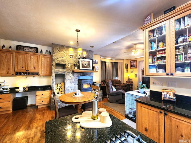 kitchen with ceiling fan with notable chandelier, dark hardwood / wood-style floors, a stone fireplace, and hanging light fixtures