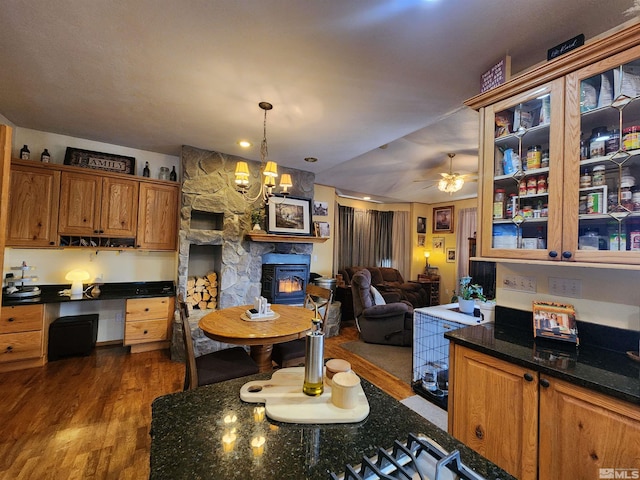 kitchen featuring pendant lighting, ceiling fan with notable chandelier, a stone fireplace, and dark wood-type flooring