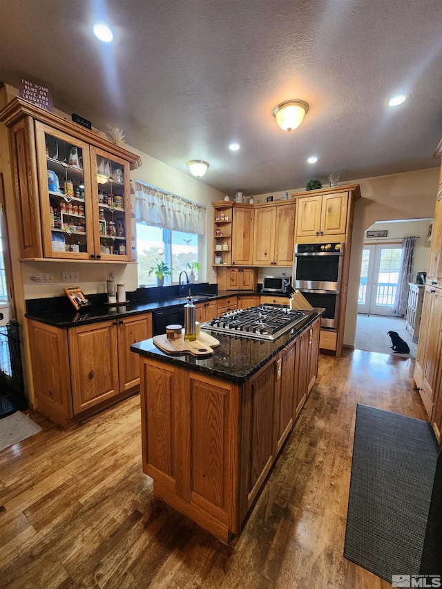 kitchen with sink, light hardwood / wood-style flooring, dark stone countertops, a kitchen island, and appliances with stainless steel finishes