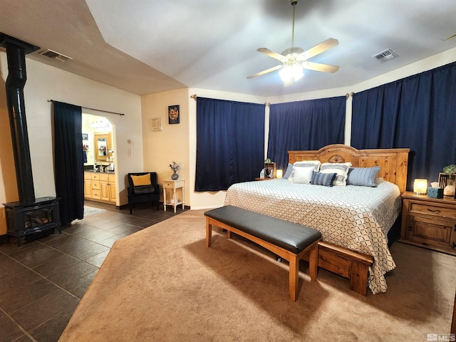 tiled bedroom featuring ceiling fan, a wood stove, and ensuite bath