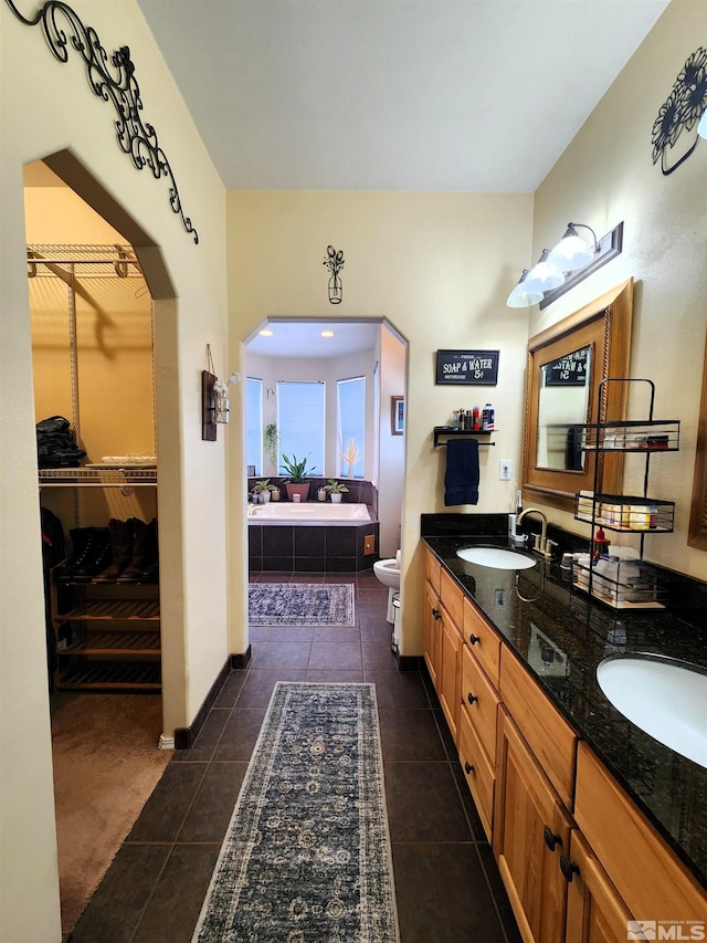 bathroom with tile patterned flooring, a relaxing tiled tub, toilet, and vanity