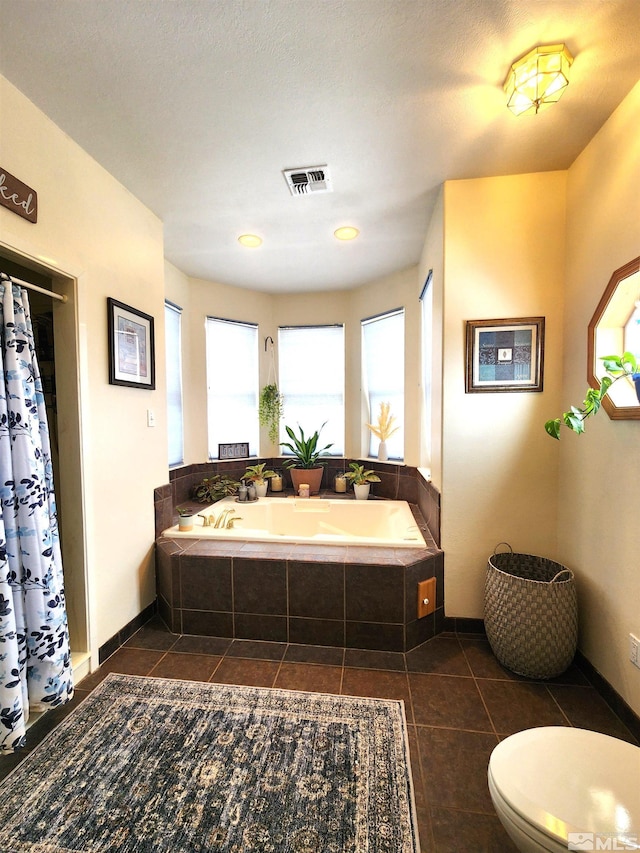 bathroom with tile patterned floors, a relaxing tiled tub, and toilet