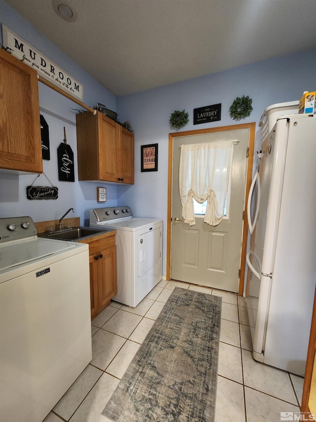 clothes washing area featuring washing machine and clothes dryer, sink, light tile patterned floors, and cabinets