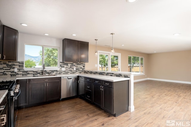 kitchen featuring sink, decorative light fixtures, dark brown cabinets, kitchen peninsula, and stainless steel appliances