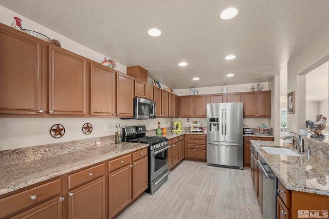 kitchen featuring a textured ceiling, light stone counters, sink, and stainless steel appliances