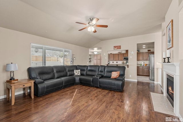 living room featuring ceiling fan, dark wood-type flooring, a tile fireplace, and vaulted ceiling