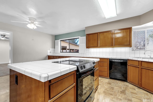 kitchen featuring tile countertops, a center island, black appliances, sink, and ceiling fan