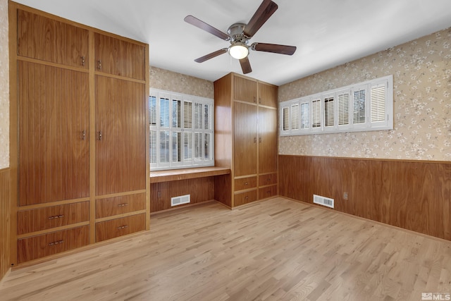 unfurnished bedroom featuring light wood-type flooring, a closet, ceiling fan, and wooden walls