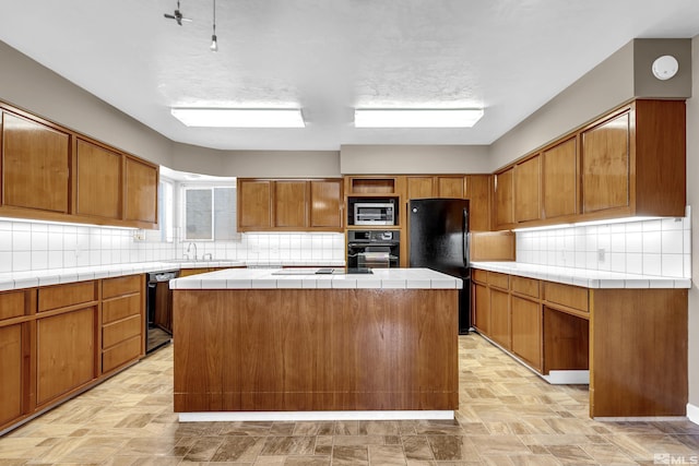 kitchen with decorative backsplash, sink, black appliances, a center island, and tile counters