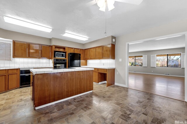 kitchen featuring decorative backsplash, tile counters, a kitchen island, and black appliances