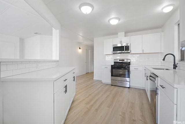 kitchen with appliances with stainless steel finishes, light hardwood / wood-style floors, white cabinetry, and sink