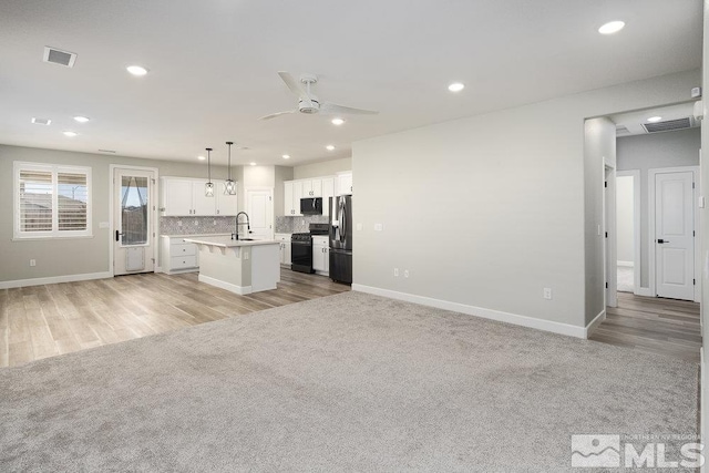 kitchen with ceiling fan, a kitchen island with sink, black appliances, pendant lighting, and white cabinets