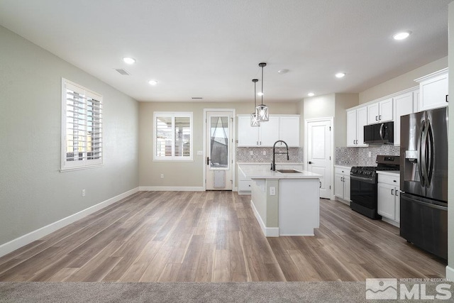 kitchen with white cabinetry, sink, an island with sink, decorative light fixtures, and black appliances