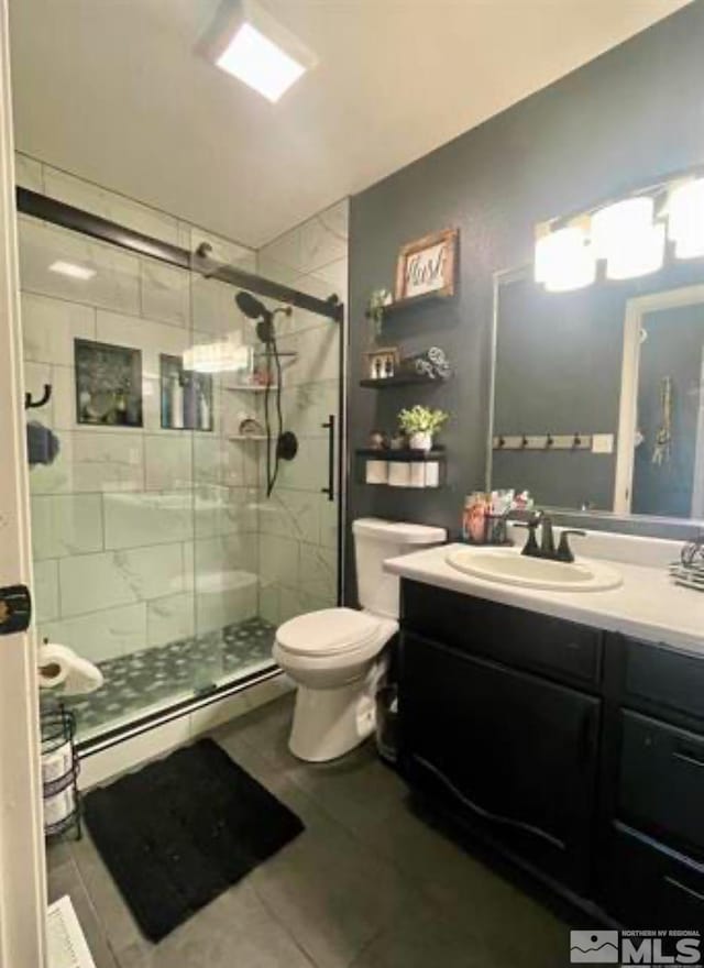 bathroom featuring baseboard heating, tile patterned flooring, toilet, a shower with door, and vanity