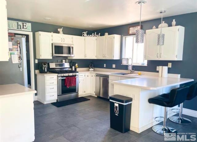 kitchen featuring kitchen peninsula, stainless steel appliances, sink, decorative light fixtures, and white cabinets