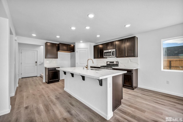 kitchen with a center island with sink, sink, stainless steel appliances, and light hardwood / wood-style flooring