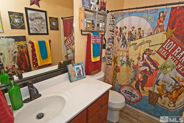 bathroom featuring wood-type flooring, vanity, toilet, and walk in shower