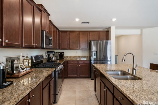 kitchen with sink, light tile patterned floors, light stone countertops, appliances with stainless steel finishes, and dark brown cabinets