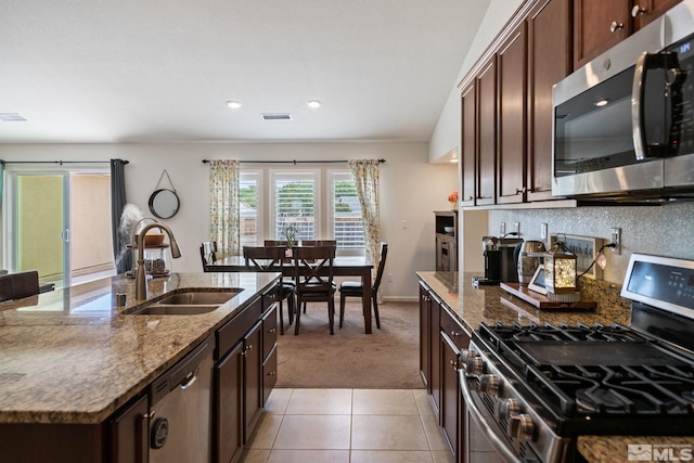 kitchen featuring light carpet, stone counters, sink, an island with sink, and stainless steel appliances