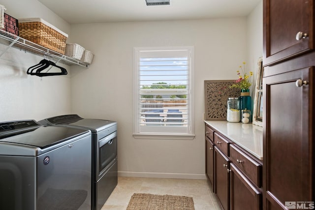 clothes washing area featuring cabinets, light tile patterned floors, and washing machine and clothes dryer