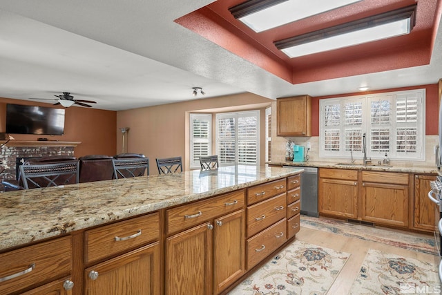 kitchen with ceiling fan, sink, a raised ceiling, stainless steel dishwasher, and light wood-type flooring