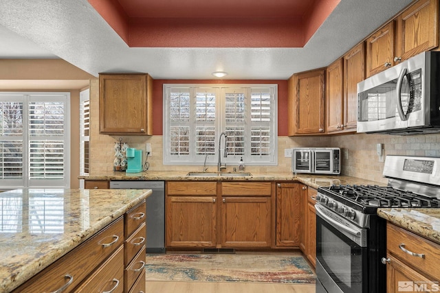 kitchen with light wood-type flooring, stainless steel appliances, light stone counters, and sink