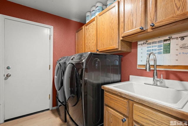 laundry room featuring washing machine and dryer, sink, cabinets, and light hardwood / wood-style flooring